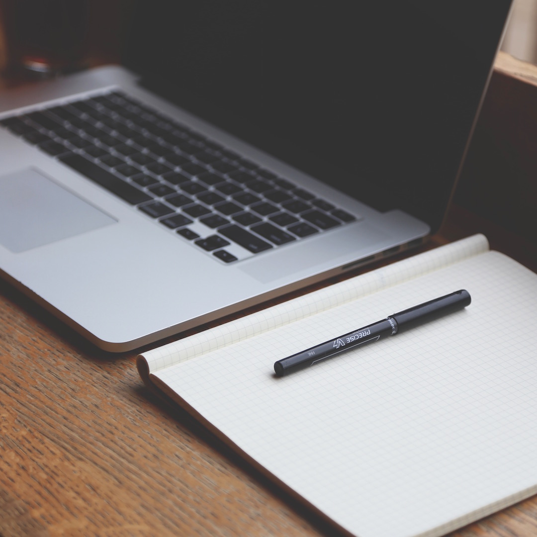 A laptop next to a paper notepad on a desk
