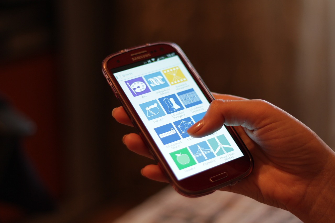 A hand holding a smartphone showing its home screen