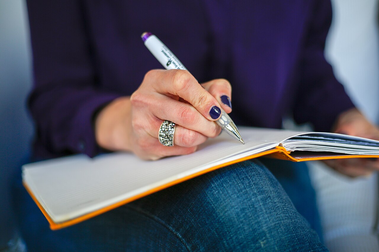 A woman writing the first line in a notebook with a pen